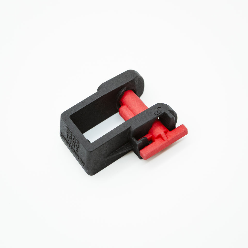 A small black plastic clamp-like component with red internal and external parts, photographed on a clean white background.